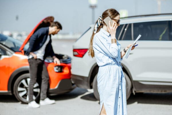 Insurance Liability Limits - Woman calling road assistance or insurance company standing on the road after the car collision, man checking the damage